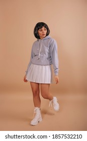 Hot girl with a bob haircut, in a hoodie and a white short skirt walking isolated beige background. Anime fan.  