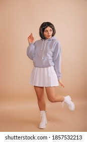 Hot girl with a bob haircut, in a hoodie and a white short skirt walking isolated beige background. Anime fan.