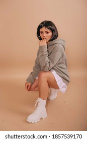 Hot girl with a bob haircut, in a hoodie and a white short skirt sitting isolated beige background. Anime fan.