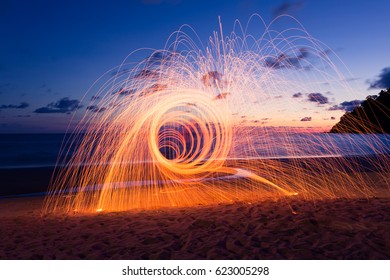 Hot Golden Sparks Flying from Man Spinning Burning Steel Wool on Wooden Bridge Extended into the Sea., Long Exposure Photography using Steel Wool Burning.