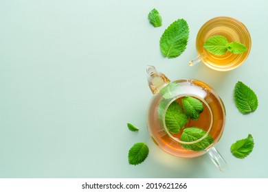 Hot green tea with mint in teapot and cup on green background. Herbal tea concept. Flat lay, top view