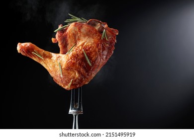 Hot grilled chicken leg sprinkled with rosemary on a black background. Chicken drumstick on a fork.