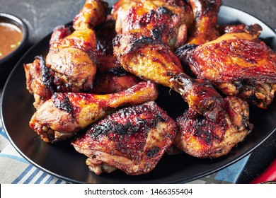 hot Grilled Jamaican Jerk Chicken drumsticks and thighs on a black plate on a concrete table, horizontal view from above, close-up