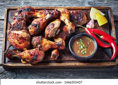 hot Grilled Jamaican Jerk Chicken on a rude board with sauce and lemon on a rustic wooden table, horizontal view from above, close-up