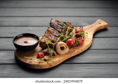 hot grilled spare ribs from a summer BBQ served with a grilled vegetables and sauce on an old vintage wooden cutting board. Copy space