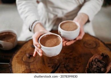 Hot handmade ceremonial cacao in white cup. Woman hands holding craft cocoa, top view on wooden table. Organic healthy chocolate drink prepared from beans, no sugar. Giving cup on ceremony, cozy cafe - Shutterstock ID 2078399830