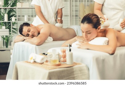 Hot herbal ball spa massage body treatment, masseur gently compresses herb bag on couple customer body. Tranquil and serenity of aromatherapy recreation in day lighting ambient at spa salon. Quiescent - Shutterstock ID 2396386585