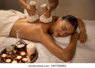 Hot herbal ball spa massage, masseur gently compresses herb bags on woman body in serenity of aromatherapy recreation in warm lighting of candles at spa salon - Powered by Shutterstock