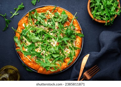 Hot homemade pizza with blue cheese, ham, pesto sauce and fresh arugula, black table background, top view