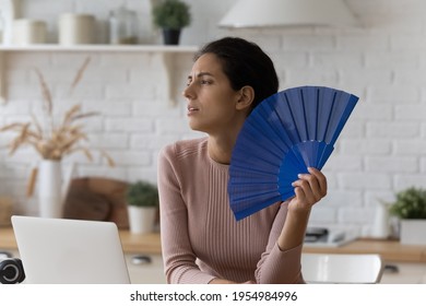 Too Hot Indoors. Exhausted Young Woman Tired Of Online Work At Home Office Suffer Breath Warm Dry Air. Millennial Latin Female Freelancer Working In Unventilated Kitchen Feel Bad Dizzy Use Hand Fan