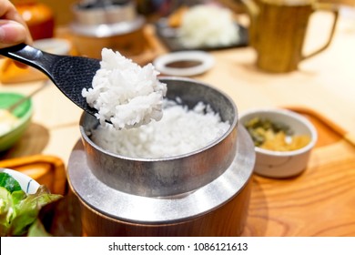 hot Japanese rice served in an old style rice cooker was pick with black plastic rice paddle.