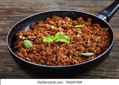 hot juicy ground beef stewed with tomato sauce, spices, basil, finely chopped vegetables and celery in frying pan, classic recipe, side view from above, close-up