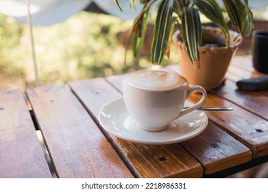 Hot Latte In White Cup On Saucer On Wooden Table And Plant Decorated In Coffee Shop