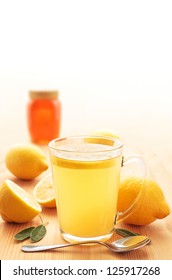 Hot Lemon Drink In A Glass Mug On Wood With Honey, Lemons And Sage Leaves