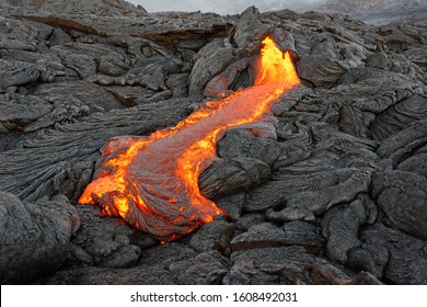 Hot magma of an active lava flow emerges from a rock fissure, the glowing lava makes the air flicker with heat, the lava cools down slowly and solidifies in bizarre patterns - Hawaii, Big Island
