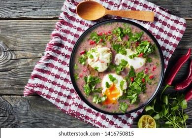 Hot Mexican Spicy Red Kidney Bean Soup With Poached Eggs And Cilantro In A Black Bowl On A Wooden Table, View From Above, Close-up, Copy Space, Flatlaym