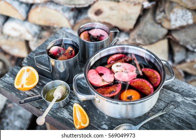 Hot Mulled Wine Outdoor In A Pot On Vintage Wooden Table - Warming Drink. Winter Or Autumn (fall) Picnic Concept. Firewood Pile As Background.