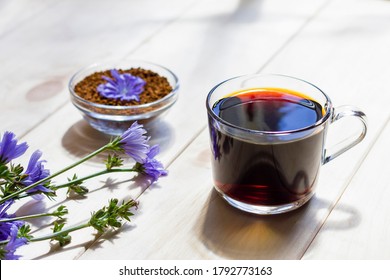 Hot natural chicory caffeine free drink in a transparent cup on a wooden table outdoors. Healthy alternative replacement for coffee, caffeine. Blue chicory flower. Beautiful summer morning at nature