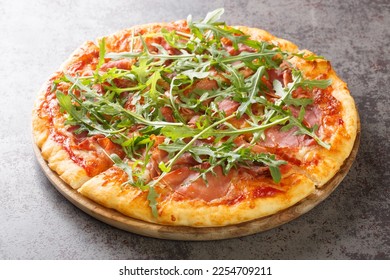 Hot pizza with prosciutto and arugula close-up on a wooden board on the table. Horizontal

