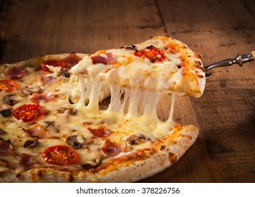 Hot pizza slice with melting cheese on a rustic wooden table.