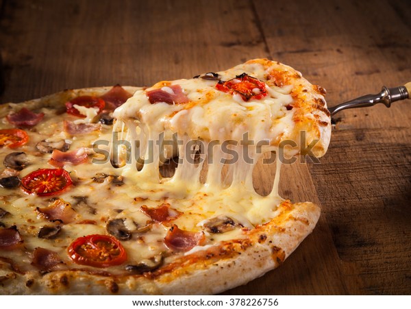 Hot pizza slice with melting cheese on a rustic\
wooden table.\
