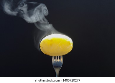 Hot potato. Fork picking up hot potato with steaming on black background.