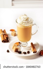 A hot pumpkin latte with spices and cinnamon stands on a white wooden table, vertical orientation.