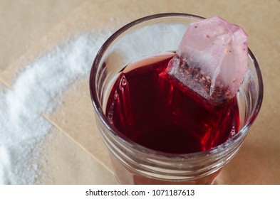 Hot Red Berry Tea And Tea Bag In Glass, Spilled Sugar Around On Bright Brown Paper Background