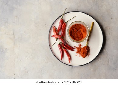 Hot Red Pepper Powder With Strucks On White Plate On Grey Background With Golden Spoon, Spice In Glass Jar With Empty Space For Text Top View