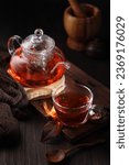 Hot red tea in a cup with the kettle on wooden table with dark background 