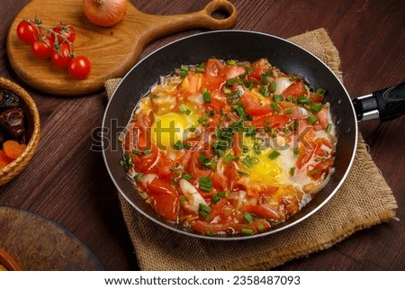 hot shakshuka in a frying pan sprinkled with green onions on the Shabbat table. Horizontal photo