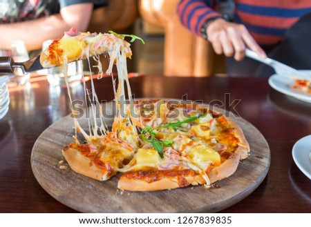 Hot Sliced Hawaiian pizza on a wooden board and the man hand taking Slices Of Pizza.