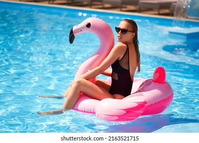 Hot Slim Female Model Posing On Inflatable Pink Flamingo Float Mattress In Bikini At Swimming Pool. Attractive Fit Woman In Swimwear Lies In The Sun On Floaty. Pretty Girl Relaxing On Tropical Vacation