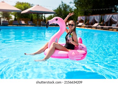 Hot Slim Woman In Bikini Chilling With Cocktail On Inflatable Pink Flamingo Float At Swimming Pool. Fit Girl In Swimwear Lies In The Sun And Drinks On Floaty. Pretty Female On Tropical Vacation.