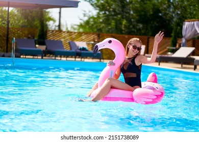 Hot Slim Woman Have Fun And Wave Hand On Inflatable Pink Flamingo Float Mattress In Bikini At Swimming Pool. Attractive Fit Girl In Swimwear Lies In Sun On Floaty. Pretty Female On Tropical Vacation.