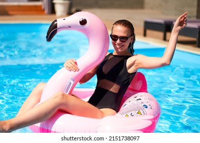 Hot Slim Woman Have Fun And Wave Hand On Inflatable Pink Flamingo Float Mattress In Bikini At Swimming Pool. Attractive Fit Girl In Swimwear Lies In Sun On Floaty. Pretty Female On Tropical Vacation.