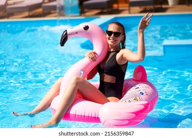 Hot Slim Woman Have Fun And Wave Hand On Inflatable Pink Flamingo Float Mattress In Bikini At Swimming Pool. Attractive Fit Girl In Swimwear Lies In Sun On Floaty. Pretty Female On Tropical Vacation.