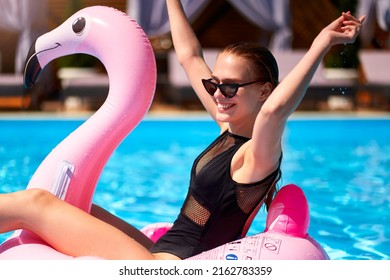 Hot Slim Woman Have Fun And Wave Hand On Inflatable Pink Flamingo Float Mattress In Bikini At Swimming Pool. Attractive Fit Girl In Swimwear Lies In Sun On Floaty. Pretty Female On Tropical Vacation.