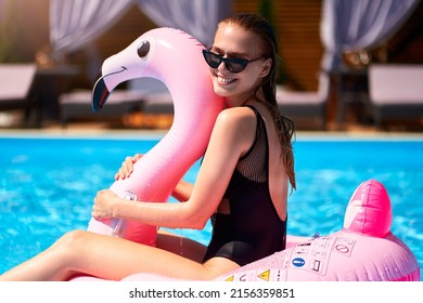 Hot Slim Woman Having Fun Laughing On Inflatable Pink Flamingo Float Mattress In Bikini At Swimming Pool. Attractive Fit Girl In Swimwear Lies In The Sun On Floaty. Pretty Female On Tropical Vacation.