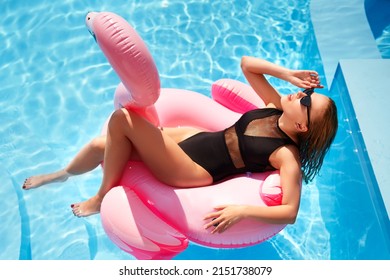 Hot Slim Woman Relaxing On Inflatable Pink Flamingo Float Mattress In Bikini At Swimming Pool. Attractive Fit Girl In Swimwear Lies In The Sun On Floaty. Pretty Female Chilling On Tropical Vacation.