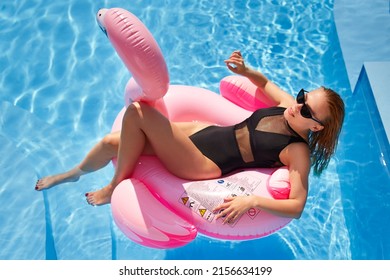 Hot Slim Woman Relaxing On Inflatable Pink Flamingo Float Mattress In Bikini At Swimming Pool. Attractive Fit Girl In Swimwear Lies In The Sun On Floaty. Pretty Female Chilling On Tropical Vacation.