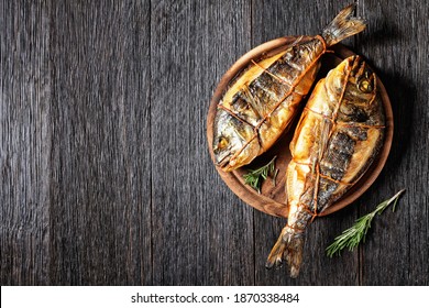 hot smoked gilt-head sea bream, orata fish on a wooden round cutting board on a dark wooden table, horizontal view from above, flat lay, free space