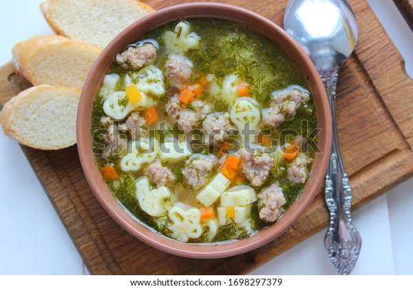 Hot soup,\
broth with meatballs, carrots, macaroni and fresh herbs.Delicious\
lunch on a wooden Board. Children\'s food, macaroni soup in the form\
of an airplane and a car.
