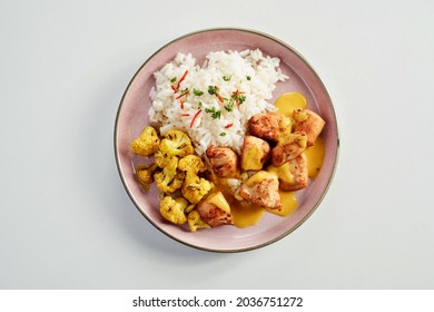 Hot spicy chicken curry with basmati rice and cauliflower florets drizzled with a tasty sauce served on a pink plate in a flat lay view on white