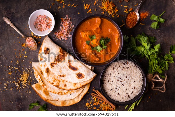 Hot spicy chicken tikka masala in bowl. Chicken curry\
with rice, indian naan butter bread, spices, herbs. Traditional\
Indian/British dish, popular indian curry in UK. Top view. Indian\
food. Close-up 