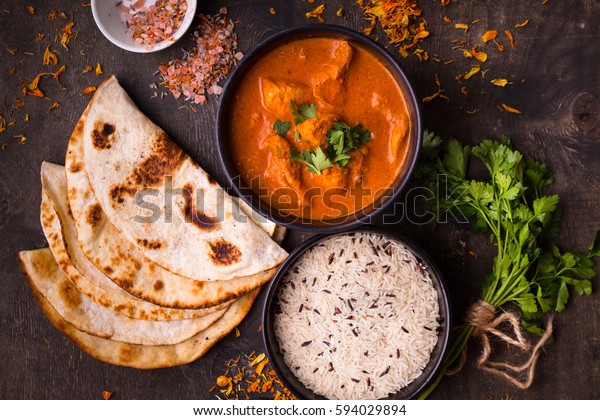 Hot spicy chicken tikka masala in bowl. Chicken curry
with rice, indian naan butter bread, spices, herbs. Traditional
Indian/British dish, popular indian curry in UK. Top view. Indian
food. Close-up 