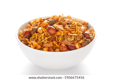 Hot spicy Nav Ratan snacks in a white bowl, made with red chili, peanuts, corn flakes, etc. Pile of Indian spicy snacks (Namkeen), under backlight, side view, against the white background.