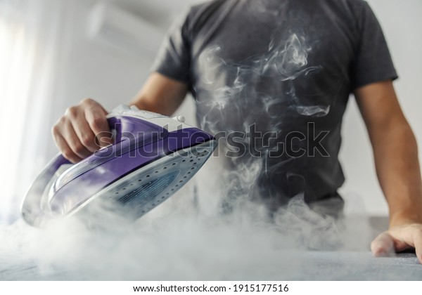 The hot steam from the iron.\
Powerful film effect of steam on photography. A close-up of a man\'s\
body in a grey t-shirt ironing clothes on an ironing\
board