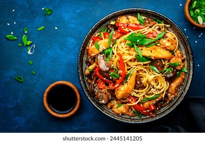 Hot stir fry egg noodles with turkey, paprika, mushrooms, chives and sesame seeds with ginger, garlic and soy sauce. Asian cuisine dish. Blue table background, top view - Powered by Shutterstock