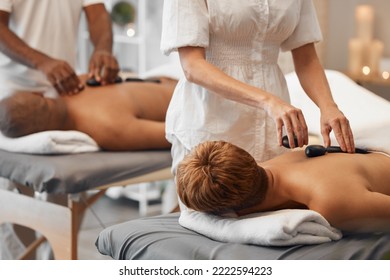 Hot Stone Massage, Black Couple And Relax Spa In Skincare Wellness, Healthcare Or Stress Management In Hotel Salon Or Resort. Woman, Man And Massage Therapist With Luxury Rock Therapy On Love Retreat